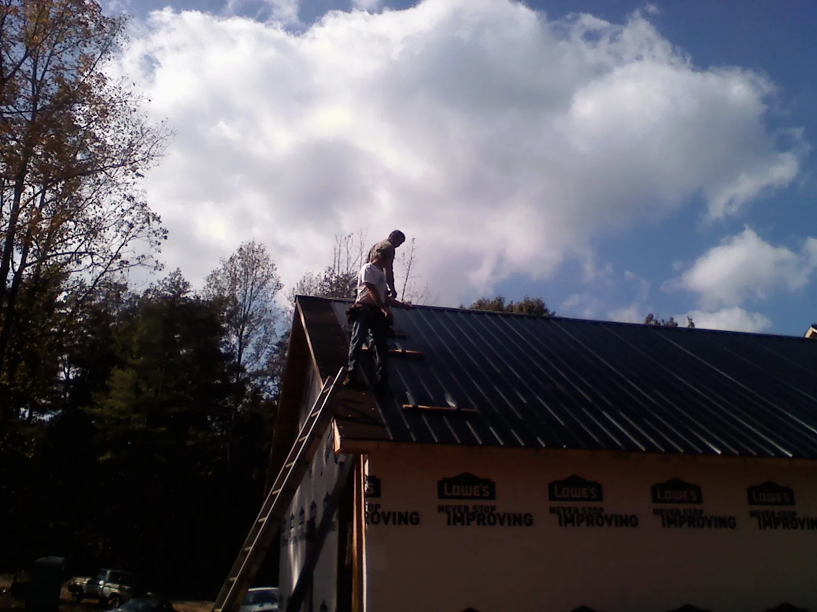 Roofer fastening dark metal panels high against a cloudy sky, from a Roof Inspection job in Red Boiling Springs