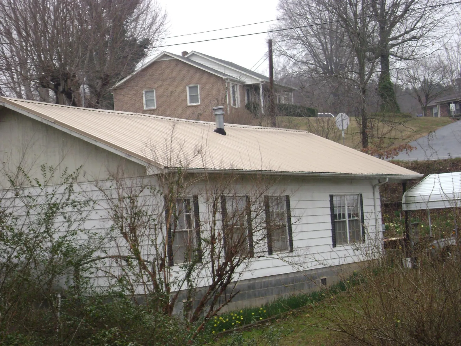 Tan metal roof on a white sided house set into a hillside — Commercial Roofing by Roofing Brothers in Red Boiling Springs